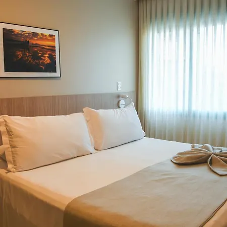 Costao Do Santinho Resort All Inclusive Florianópolis Habitación foto This is a photograph of a bright and comfortable hotel or bedroom setting.

The main focus is a large, neatly made bed with white linens. There are four pillows visible, two sets of which are arranged at the head of the bed. A light-colored throw or 