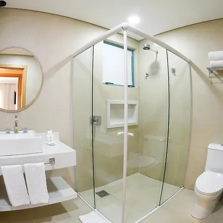 Costao Do Santinho Resort All Inclusive Florianópolis Habitación foto This is an image of a modern and clean bathroom.

**Key features visible in the photo include:**

*   **Vanity Area:** On the left, there is a white, floating vanity with a built-in sink. A circular mirror hangs above the sink. Towels are neatly fold
