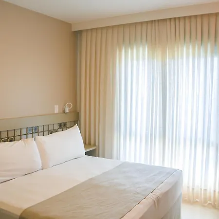 Costao Do Santinho Resort All Inclusive Florianópolis Habitación foto This is an image of a bright, modern bedroom, likely in a hotel or rental apartment.

**Key features of the photo:**

*   **Bed:** A large, neatly made bed dominates the foreground. It has crisp white linens, topped with several white pillows. A ligh